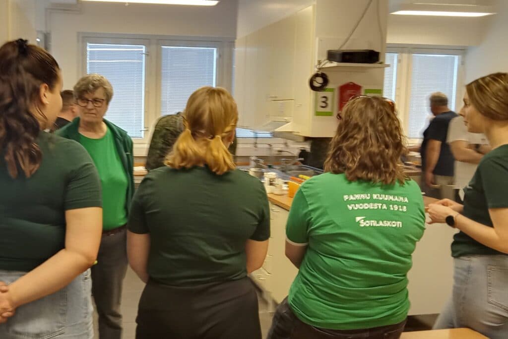 Nuoret sotilaskotisisaret valvovat kokkisotaa, jossa tehdään vohveleita ja vatkataan kermaa käsin. Herrasmieskisaan Sotilaskotiyhdistys on kutsuttu veteraanijärjestöjen tilalle.